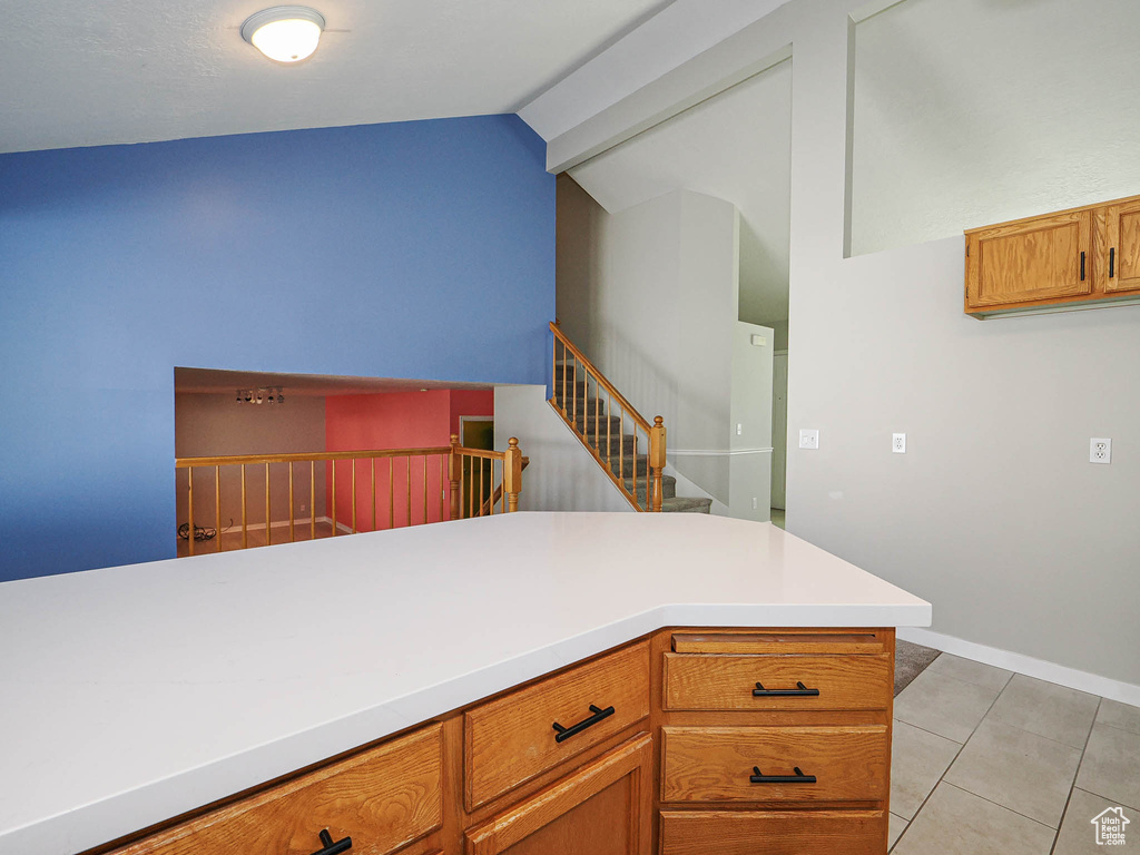 Kitchen featuring lofted ceiling, light tile patterned floors, light countertops, brown cabinets, and baseboards