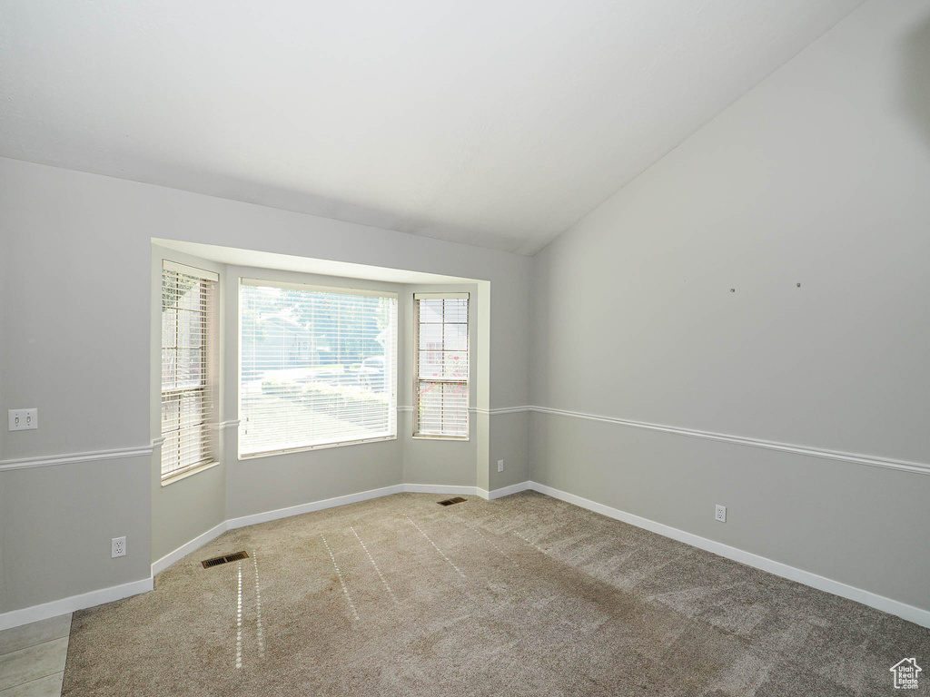 Unfurnished room with vaulted ceiling, baseboards, and light carpet