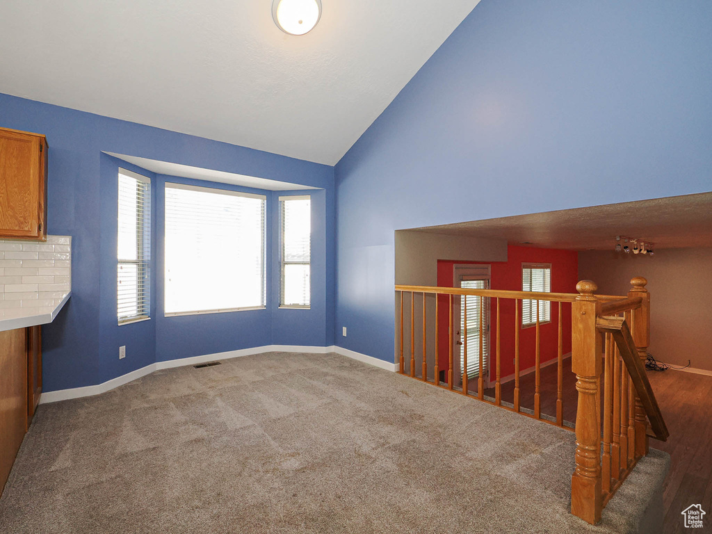 Unfurnished room with baseboards, high vaulted ceiling, and carpet floors