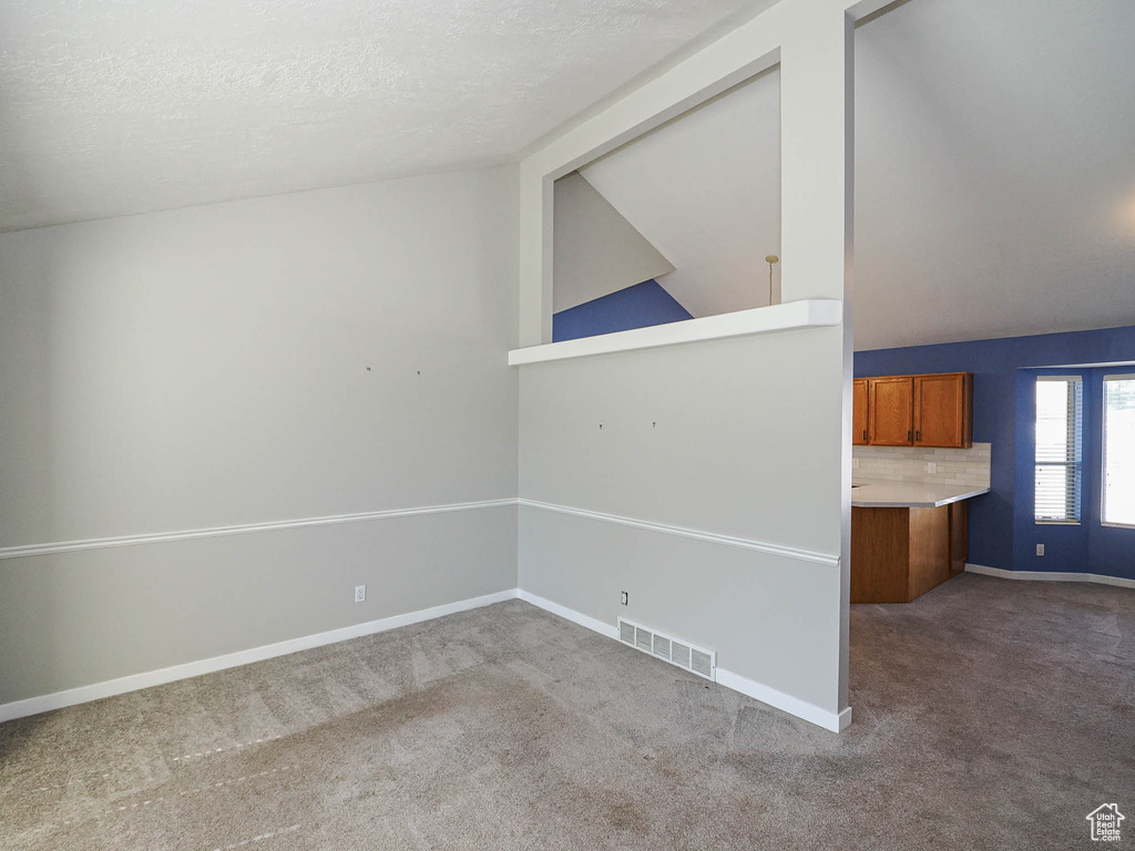 Carpeted spare room with baseboards, a textured ceiling, and lofted ceiling