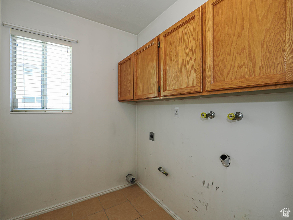 Laundry area featuring gas dryer hookup, cabinet space, light tile patterned floors, baseboards, and hookup for an electric dryer