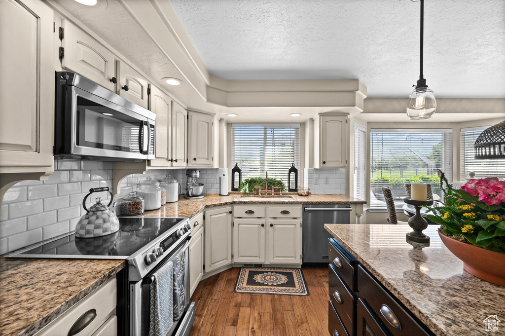 Kitchen featuring stainless steel appliances, dark wood-type flooring, a textured ceiling, a sink, and decorative light fixtures