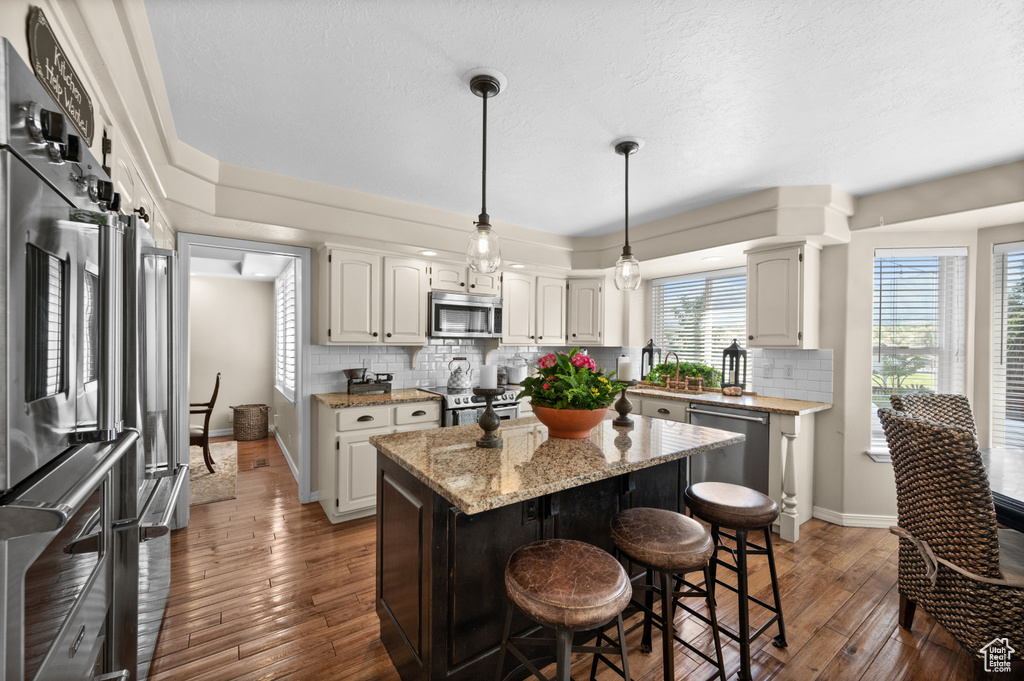Kitchen featuring stainless steel appliances, wood-type flooring, tasteful backsplash, a center island, and a textured ceiling