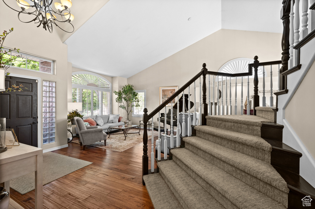 Foyer entrance with high vaulted ceiling, stairway, dark wood-style flooring, and a chandelier