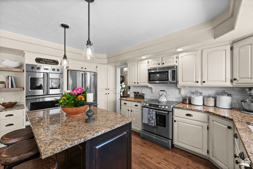 Kitchen featuring appliances with stainless steel finishes, a breakfast bar area, dark wood finished floors, white cabinets, and light stone countertops