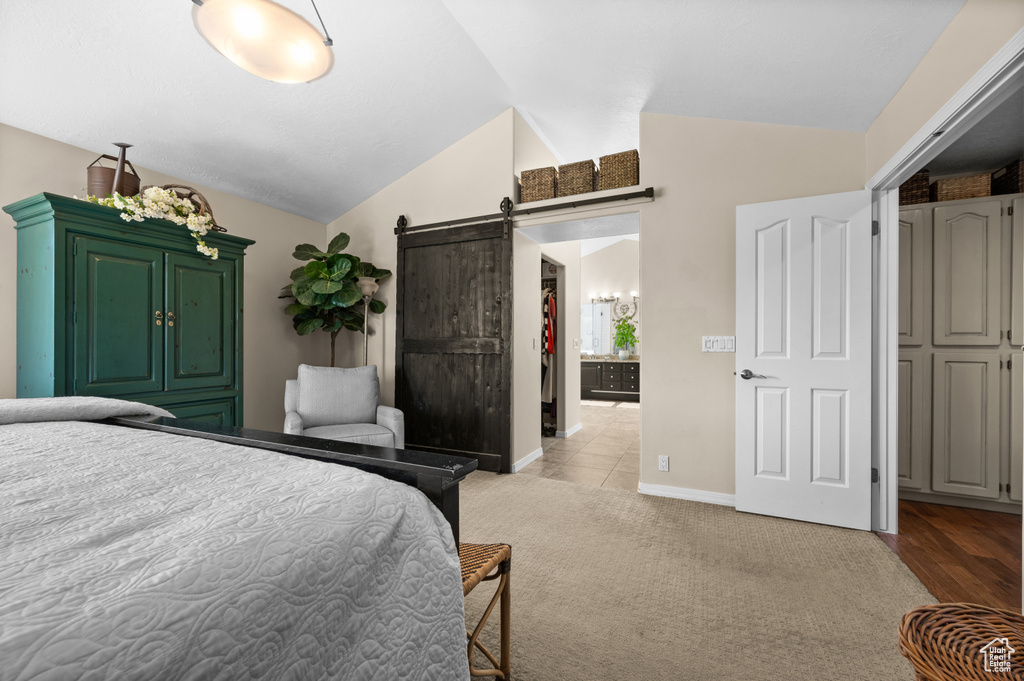 Bedroom featuring a barn door, vaulted ceiling, and baseboards