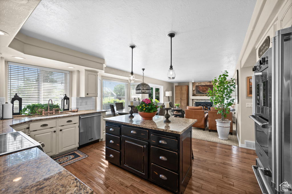 Kitchen featuring dishwasher, a sink, a stone fireplace, dark wood-style flooring, and white cabinets