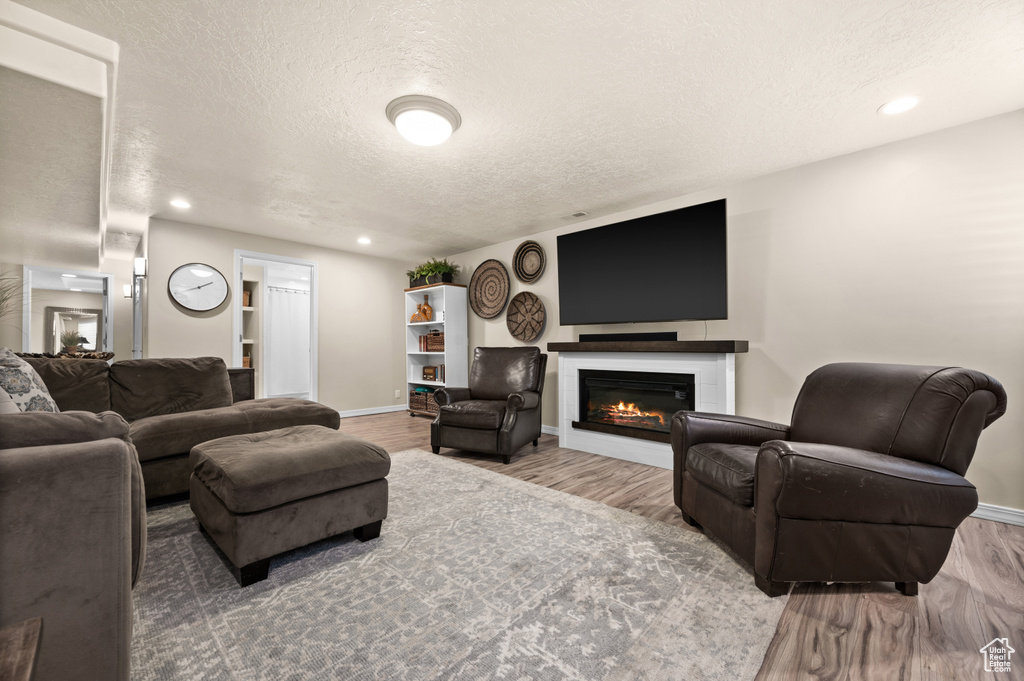 Living area featuring wood finished floors, a textured ceiling, a glass covered fireplace, baseboards, and recessed lighting