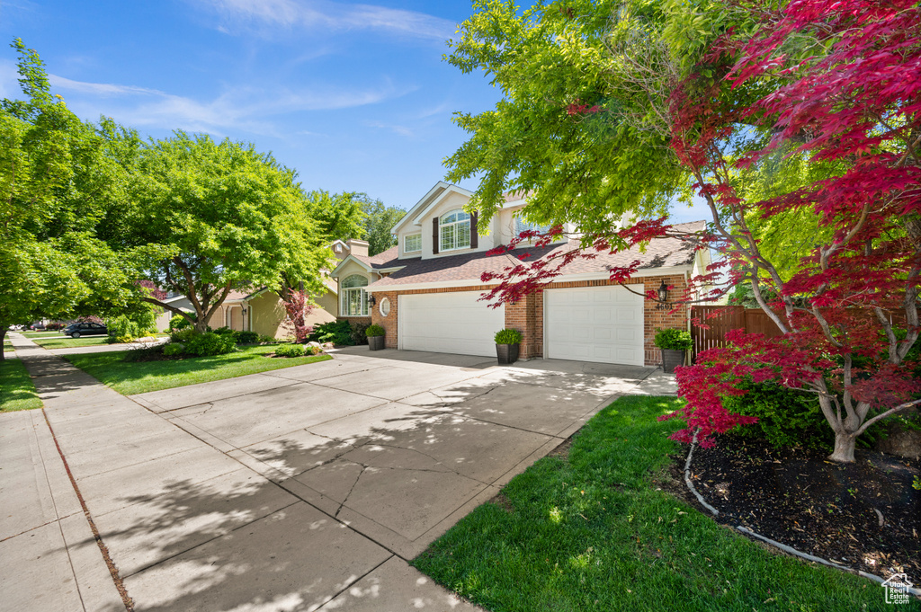 View of front of property with concrete driveway, an attached garage, brick siding, and a front lawn