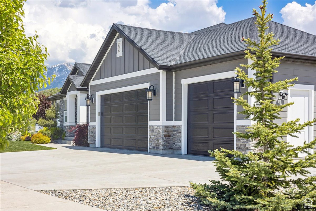 View of home's exterior with a garage, board and batten siding, driveway, a shingled roof, and stone siding