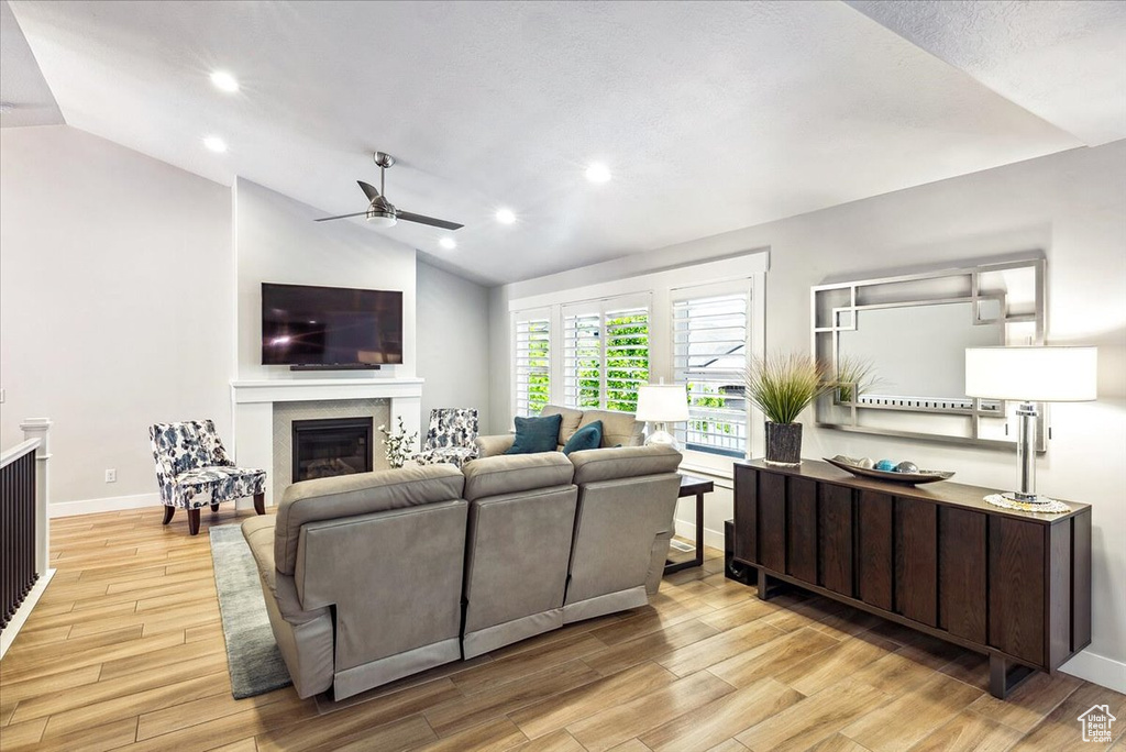 Living room with lofted ceiling, ceiling fan, a glass covered fireplace, light wood-style floors, and recessed lighting