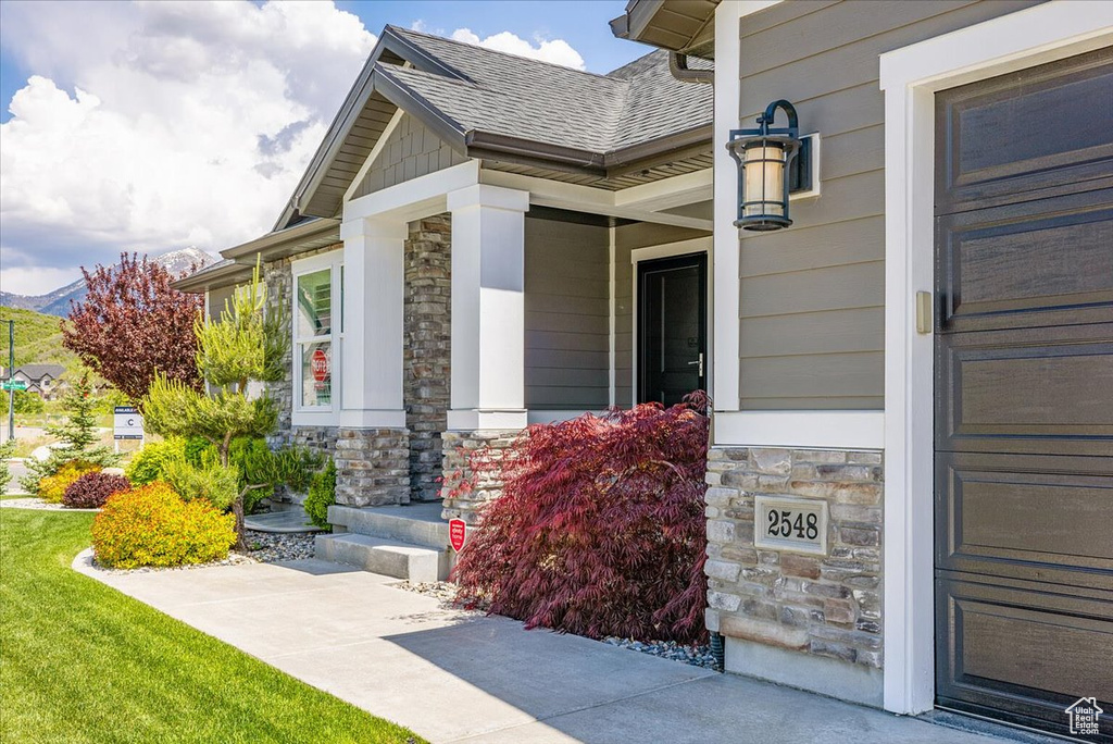View of exterior entry featuring stone siding, a porch, a shingled roof, and a mountain view
