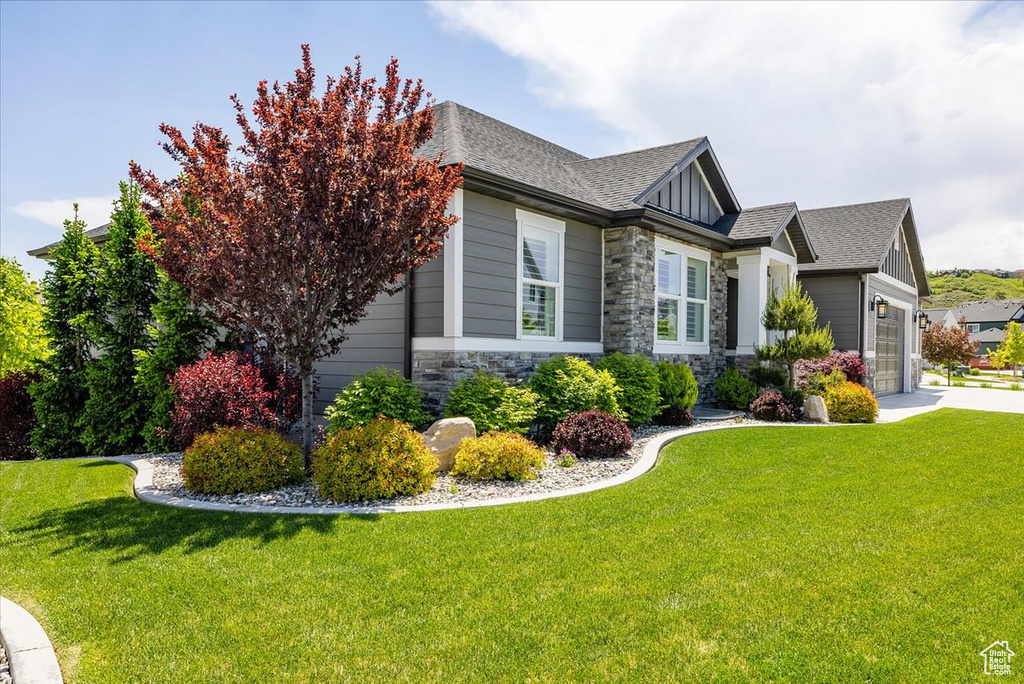 View of property exterior with an attached garage, stone siding, a yard, and roof with shingles