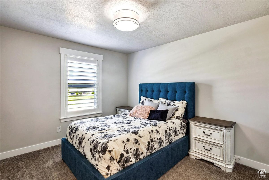 Bedroom with dark carpet, a textured ceiling, and baseboards