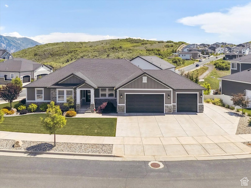 Craftsman inspired home featuring stone siding, an attached garage, concrete driveway, a front lawn, and board and batten siding