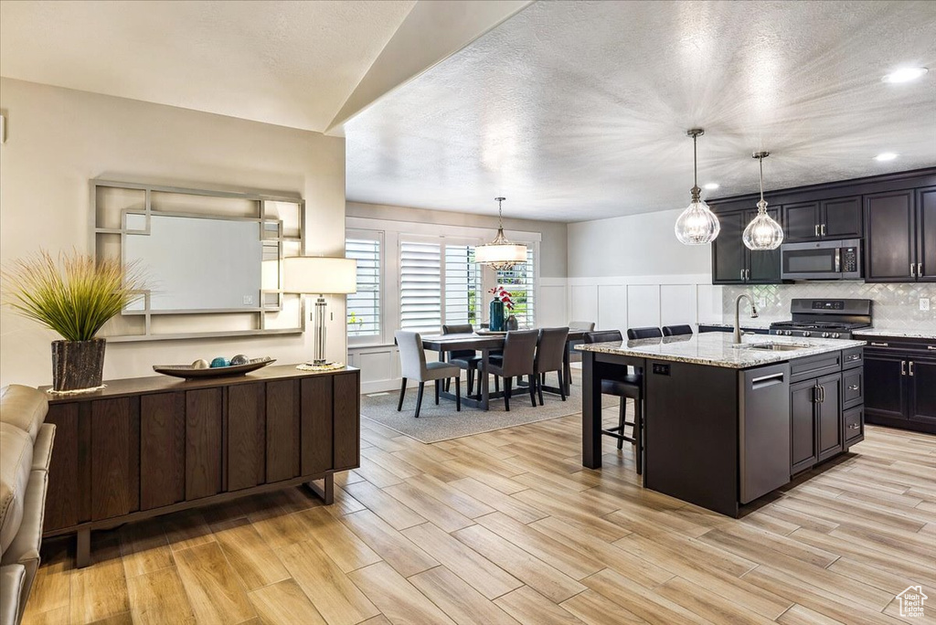 Kitchen with appliances with stainless steel finishes, a sink, light wood-style floors, light stone counters, and recessed lighting