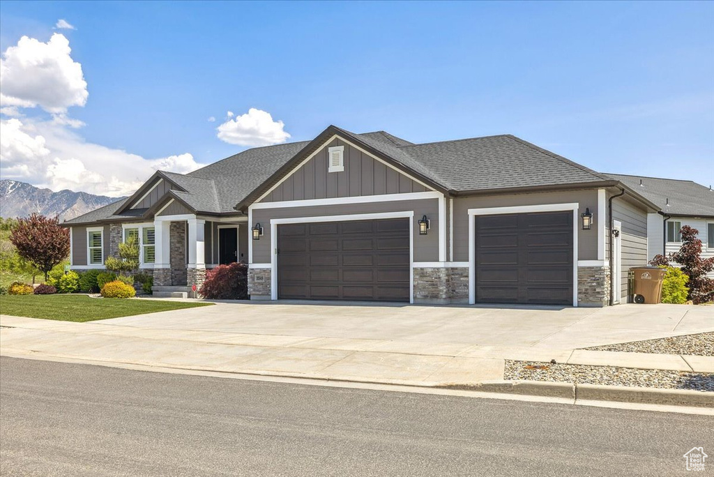 Craftsman-style home with a garage, concrete driveway, stone siding, a shingled roof, and board and batten siding