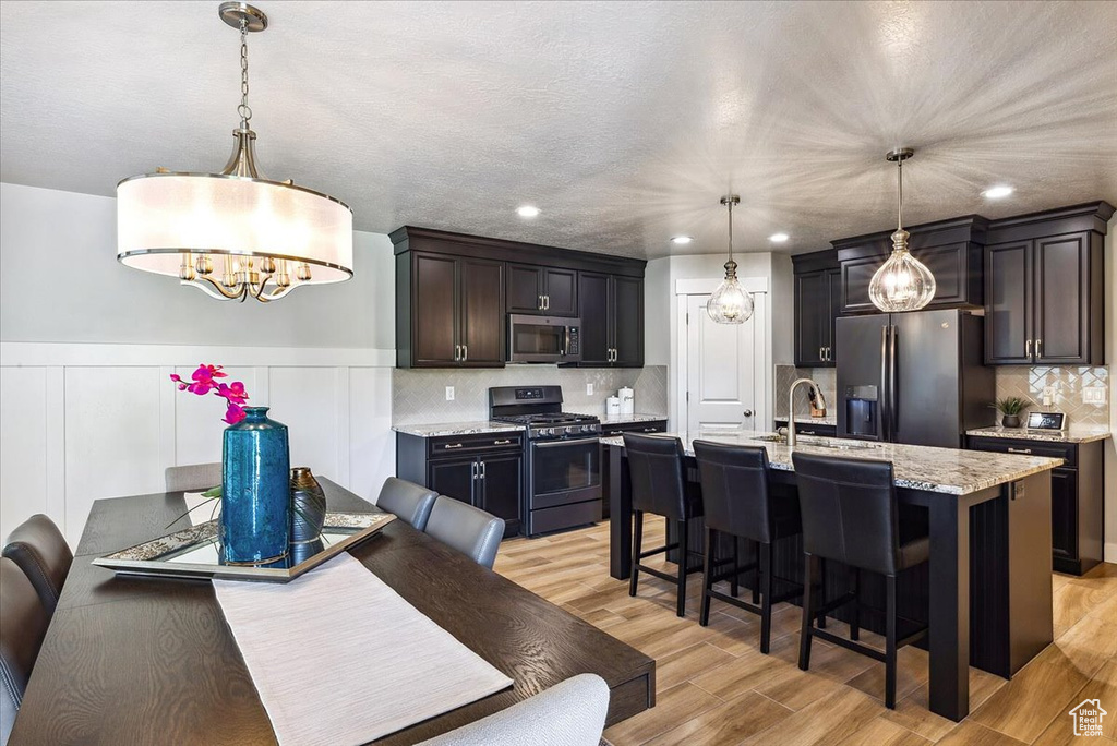 Kitchen with appliances with stainless steel finishes, a chandelier, light wood-style floors, a breakfast bar area, and a sink