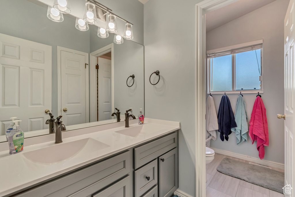 Full bathroom featuring double vanity, toilet, and baseboards