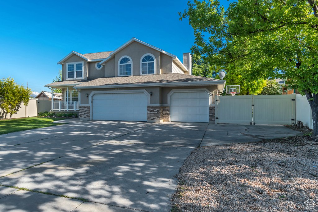 Traditional-style house featuring a gate, driveway, stucco siding, a chimney, and a garage