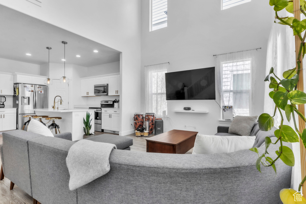 Living area featuring light wood finished floors, plenty of natural light, a high ceiling, and recessed lighting