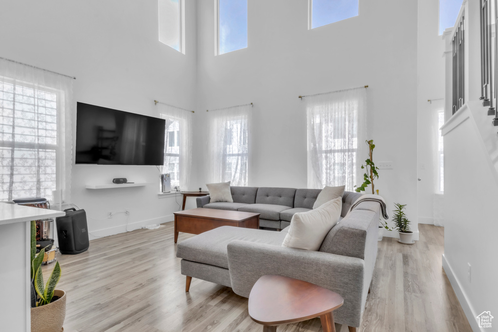 Living area with a high ceiling, light wood-style flooring, healthy amount of natural light, and baseboards