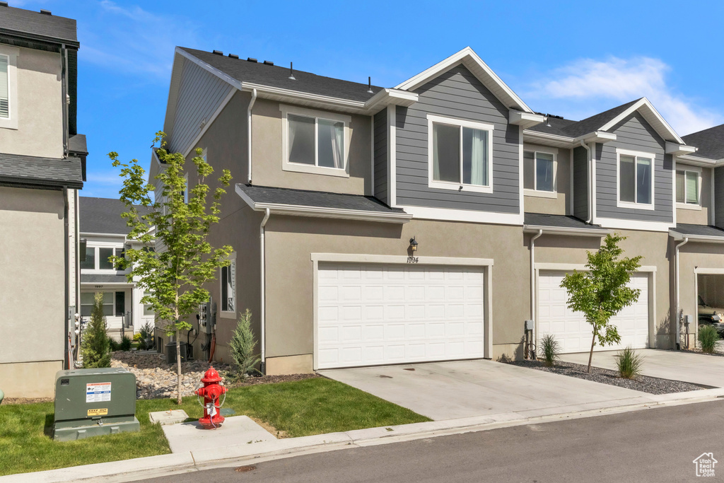 View of front of home featuring an attached garage, stucco siding, concrete driveway, and central AC