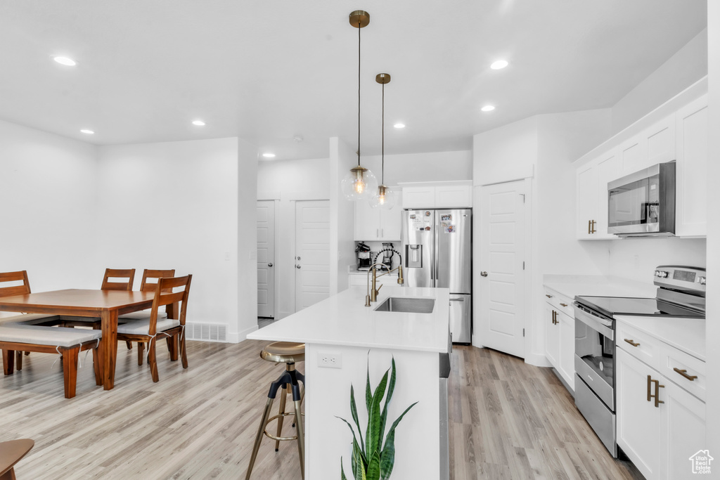 Kitchen with appliances with stainless steel finishes, a sink, light wood finished floors, a breakfast bar area, and recessed lighting