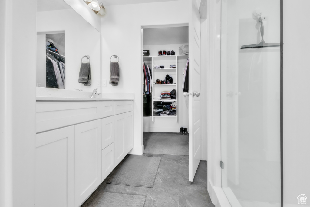 Bathroom featuring vanity, a walk in closet, a shower stall, and concrete flooring