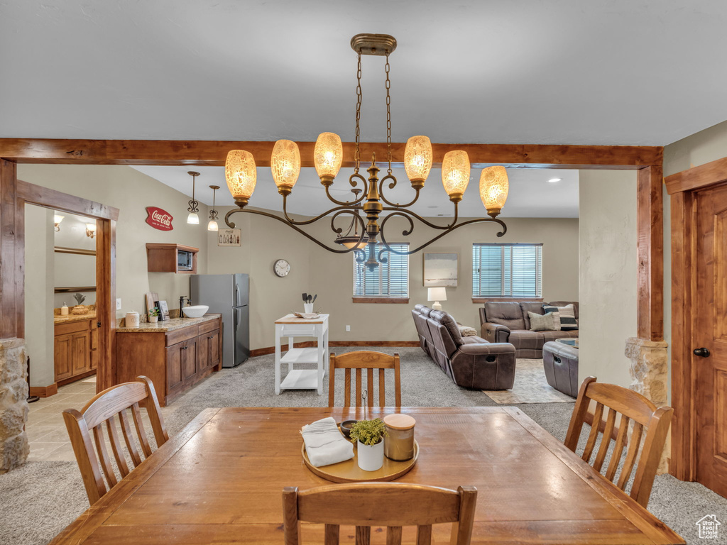 Dining room with light colored carpet, a chandelier, beamed ceiling, and baseboards