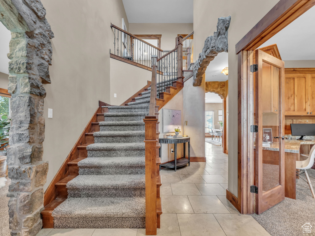 Stairs with plenty of natural light, a high ceiling, tile patterned floors, and arched walkways