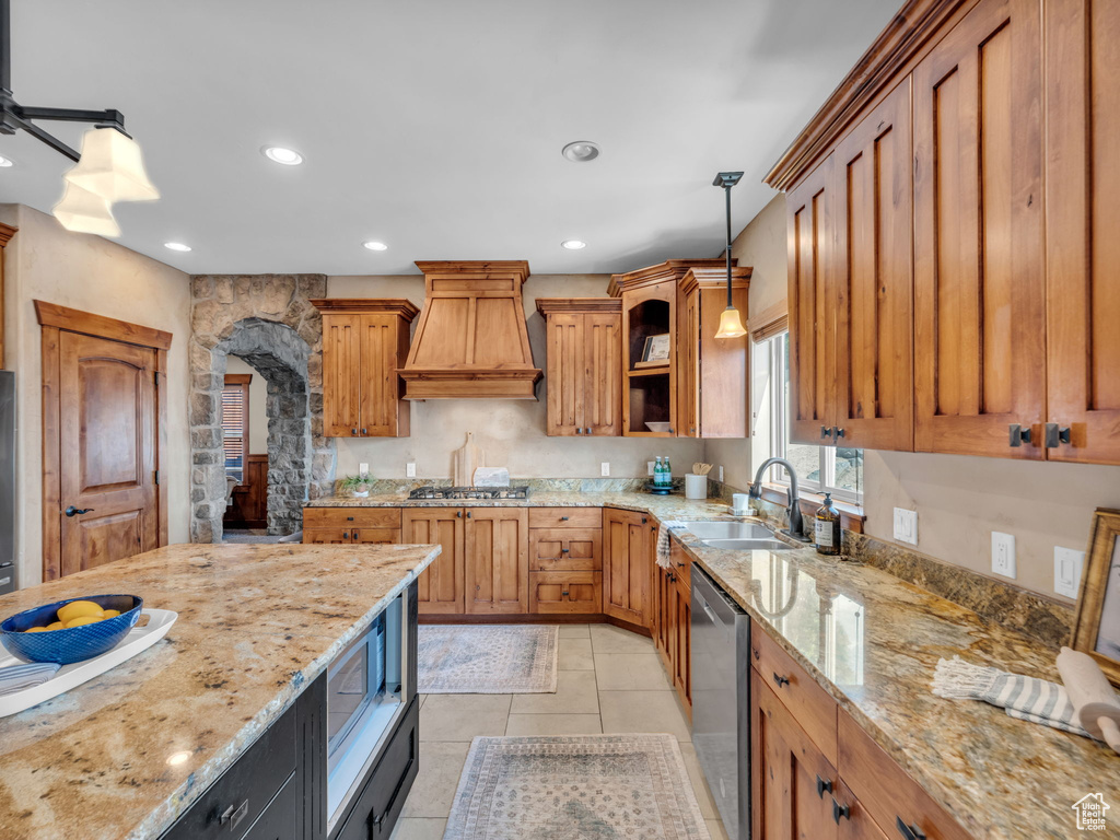 Kitchen with a sink, stainless steel appliances, custom range hood, decorative light fixtures, and light stone countertops