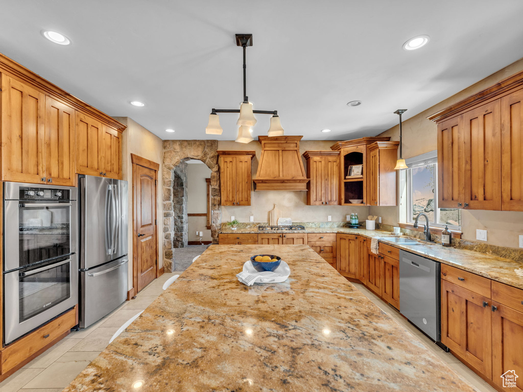 Kitchen featuring stainless steel appliances, premium range hood, light stone countertops, a sink, and recessed lighting