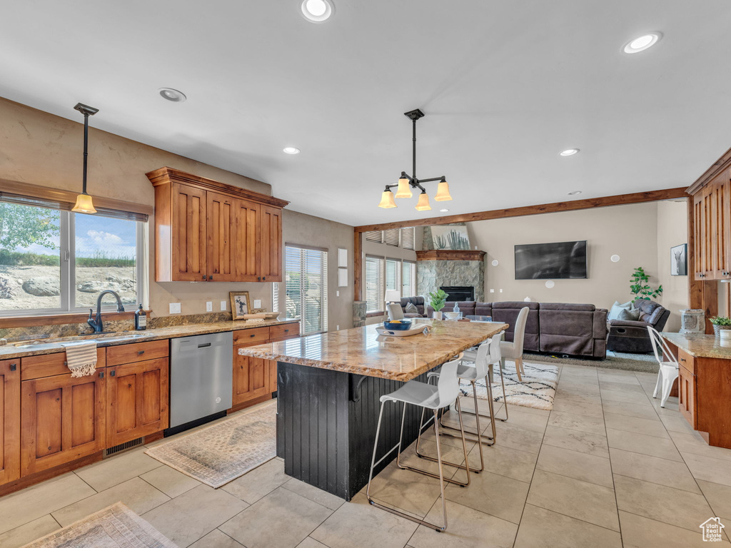 Kitchen with stainless steel dishwasher, light stone countertops, a sink, a center island, and brown cabinets
