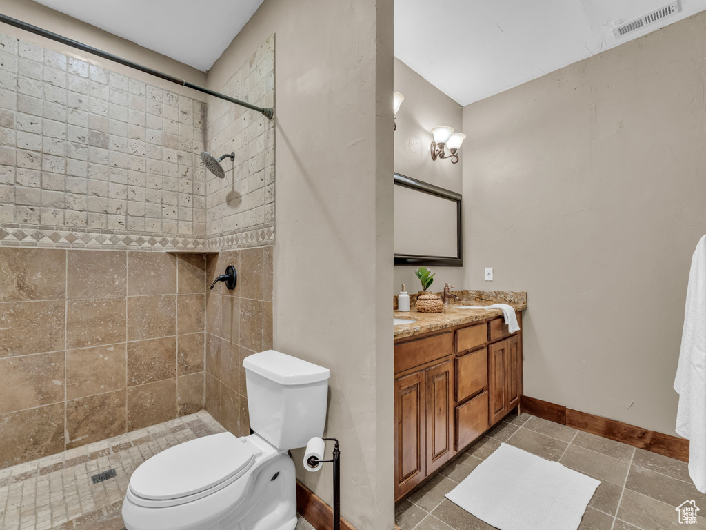 Bathroom with double vanity, toilet, baseboards, tiled shower, and tile patterned flooring