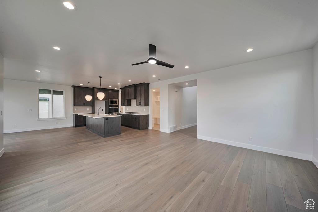 Kitchen featuring open floor plan, a center island with sink, light countertops, dark brown cabinets, and wood finished floors