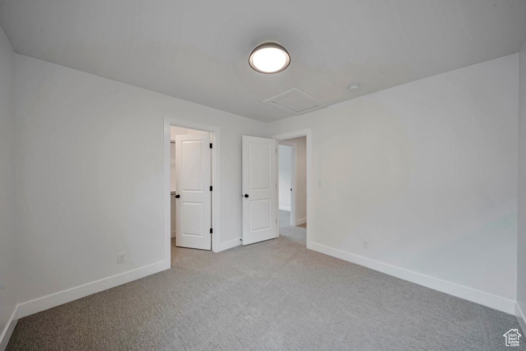 Unfurnished bedroom featuring light colored carpet, attic access, and baseboards