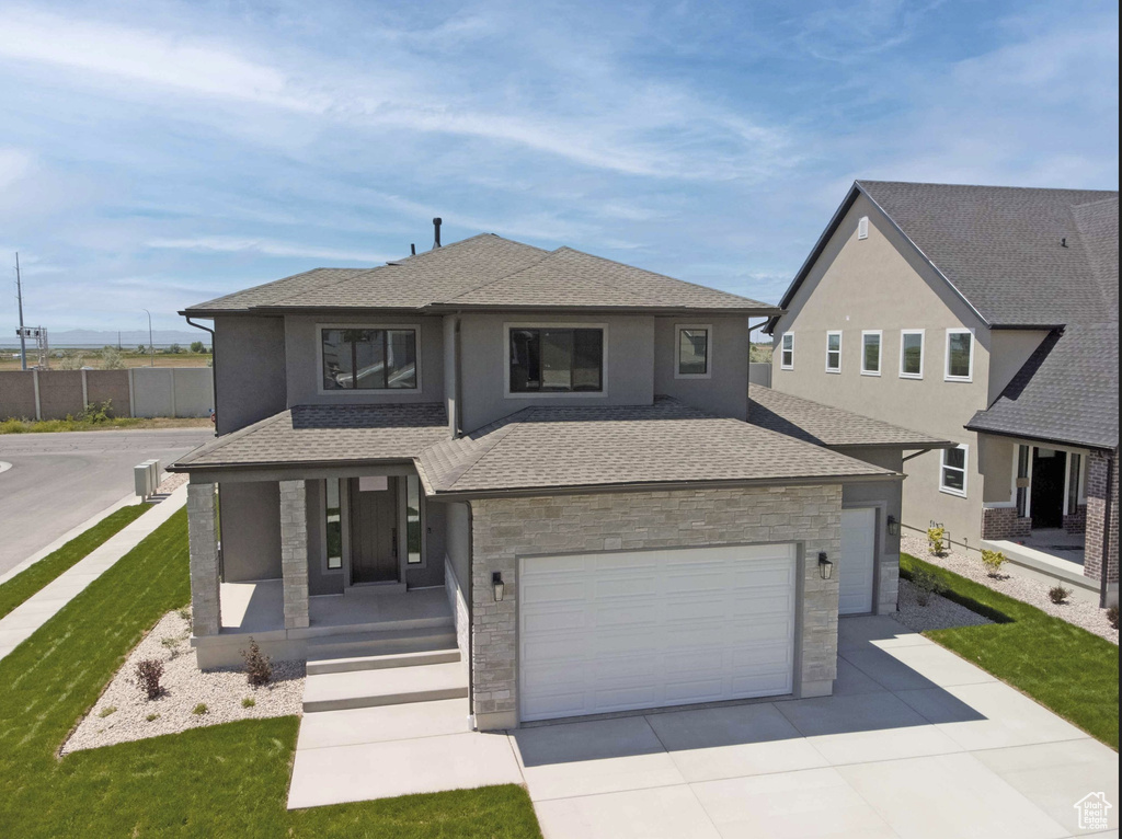 View of front of property featuring covered porch, driveway, stone siding, and a shingled roof