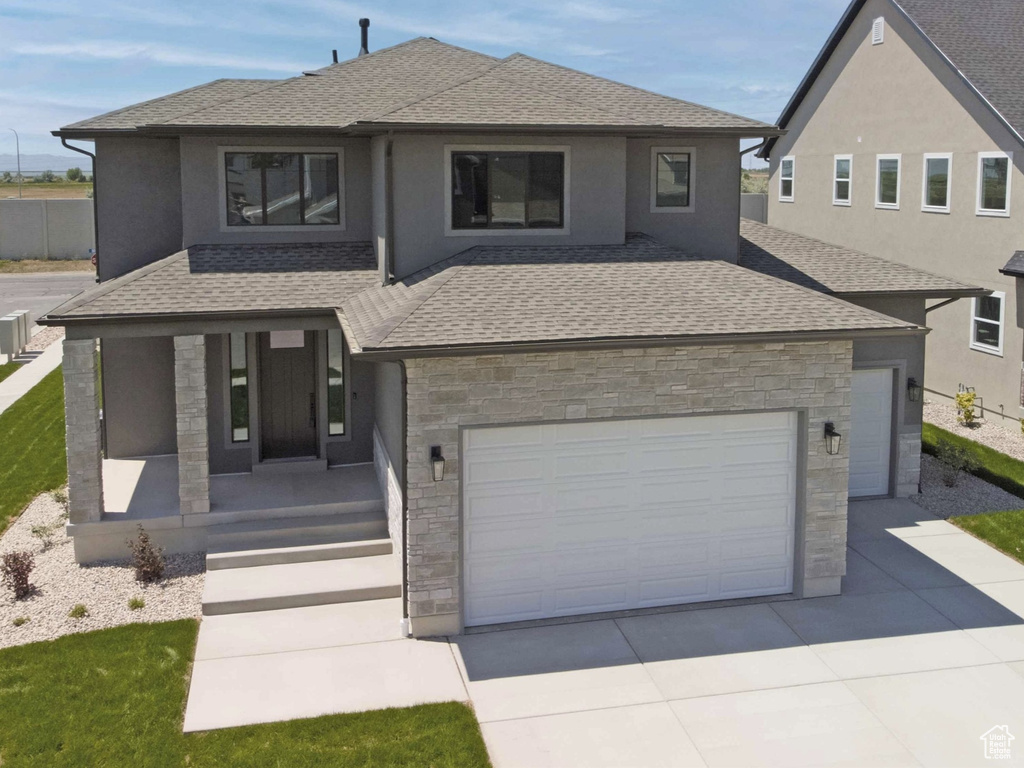 View of front of property featuring covered porch, driveway, stone siding, and a shingled roof