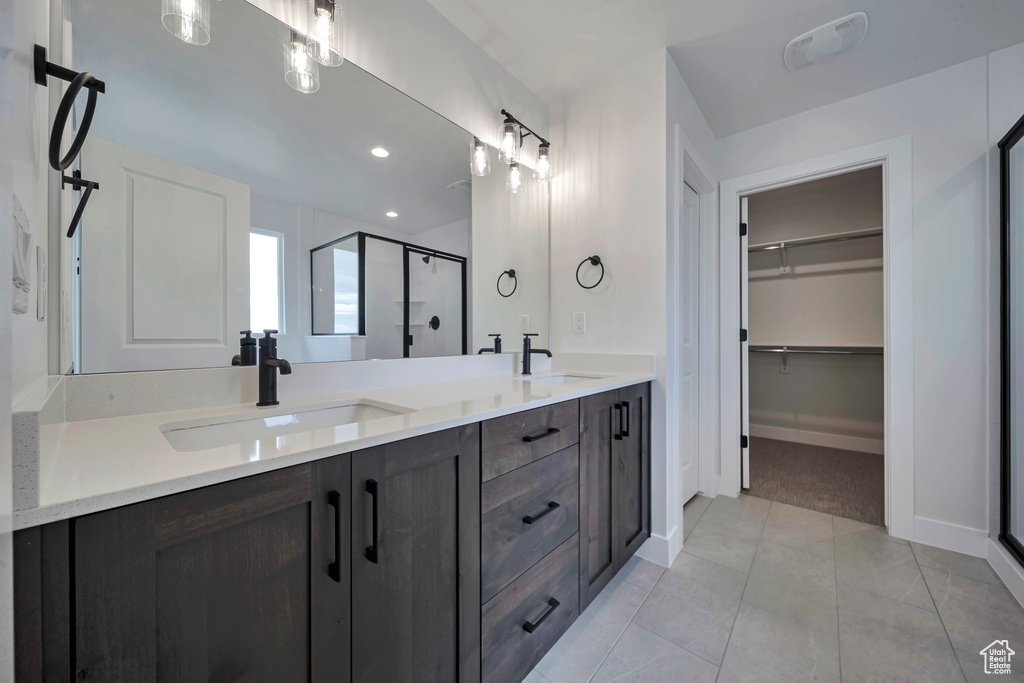Bathroom with a shower stall, double vanity, a walk in closet, baseboards, and recessed lighting