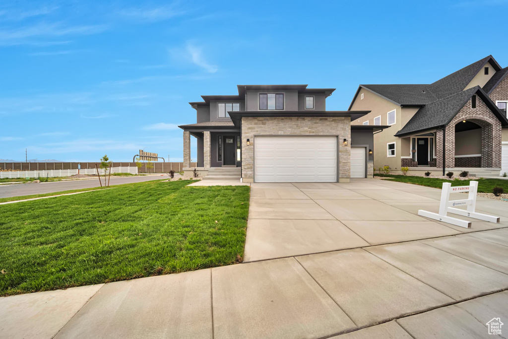 View of front of home featuring stone siding, a front yard, driveway, an attached garage, and stucco siding