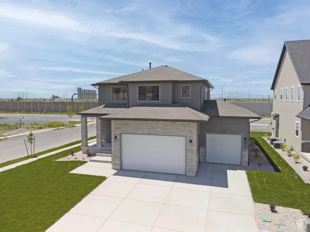 View of front of property with stone siding, concrete driveway, a shingled roof, a garage, and stucco siding