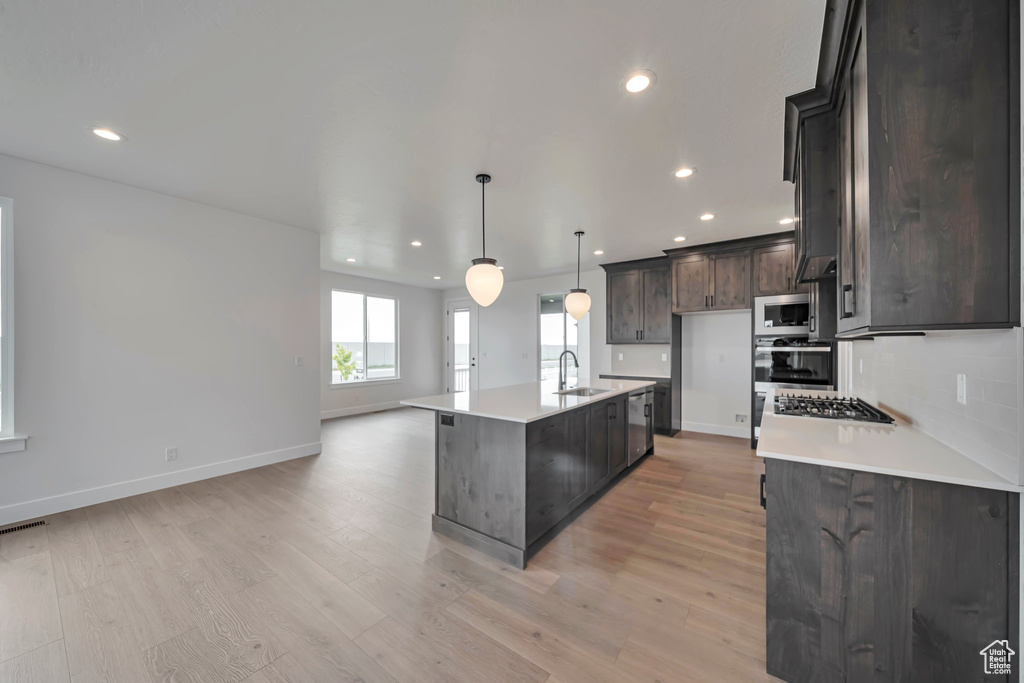 Kitchen with a sink, appliances with stainless steel finishes, recessed lighting, light wood finished floors, and baseboards