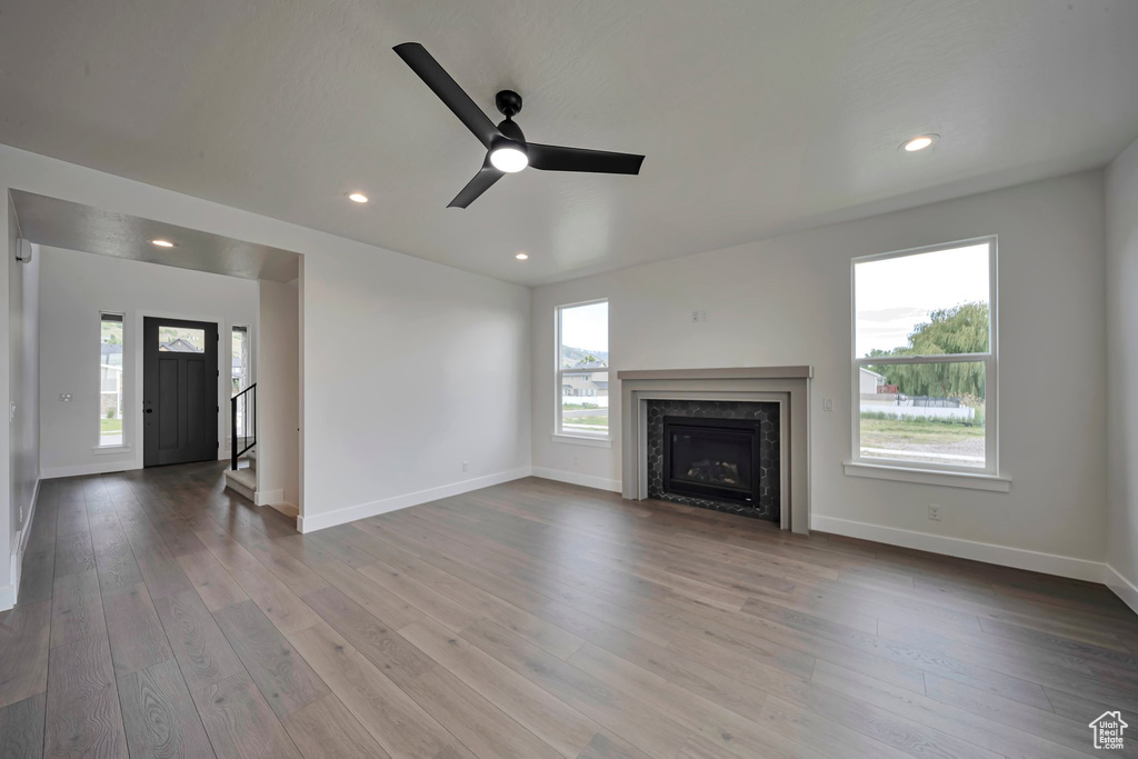 Unfurnished living room featuring ceiling fan, a premium fireplace, baseboards, wood finished floors, and recessed lighting