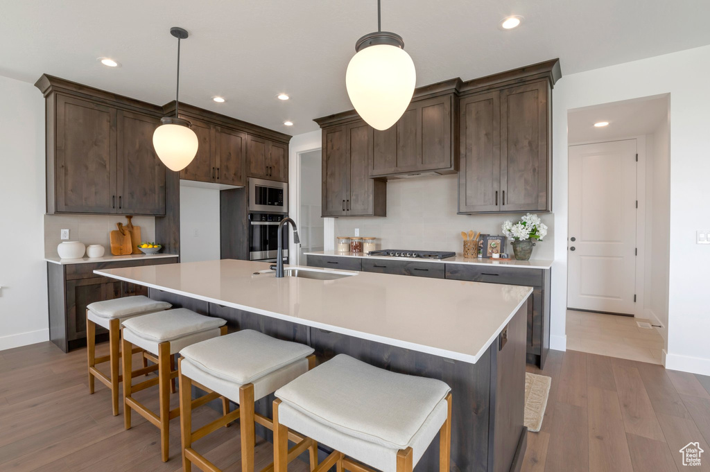 Kitchen featuring stainless steel appliances, dark brown cabinets, light countertops, recessed lighting, and wood finished floors