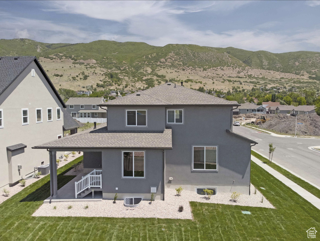 Rear view of property featuring stucco siding, a shingled roof, a mountain view, and a yard