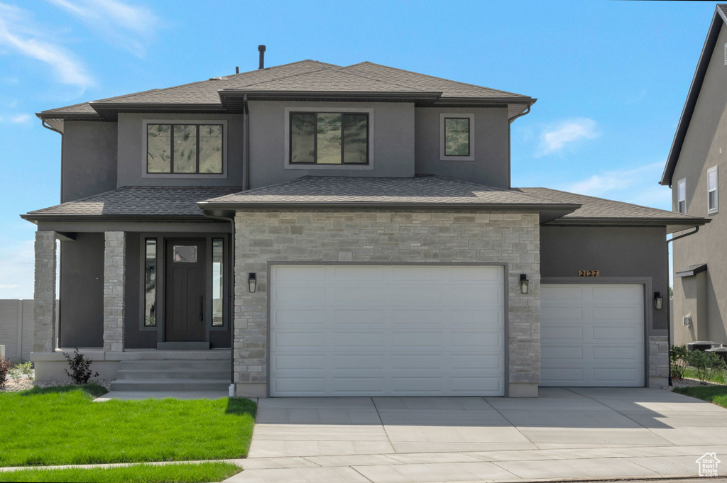 Prairie-style house featuring stone siding, driveway, an attached garage, a front yard, and stucco siding