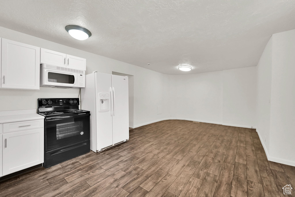Kitchen featuring white appliances, dark wood-style floors, white cabinetry, baseboards, and a textured ceiling