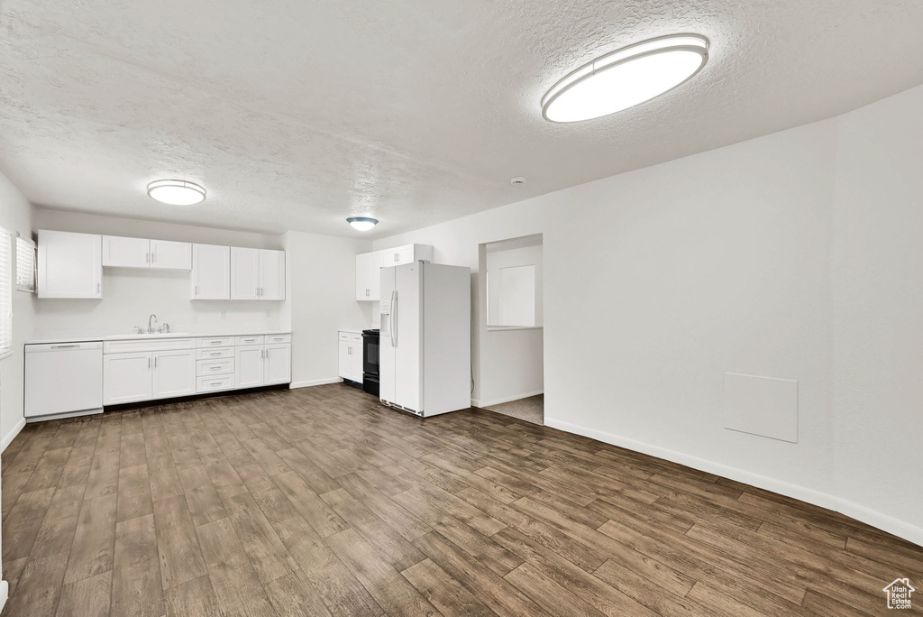 Unfurnished living room featuring a textured ceiling, dark wood-type flooring, baseboards, and a sink