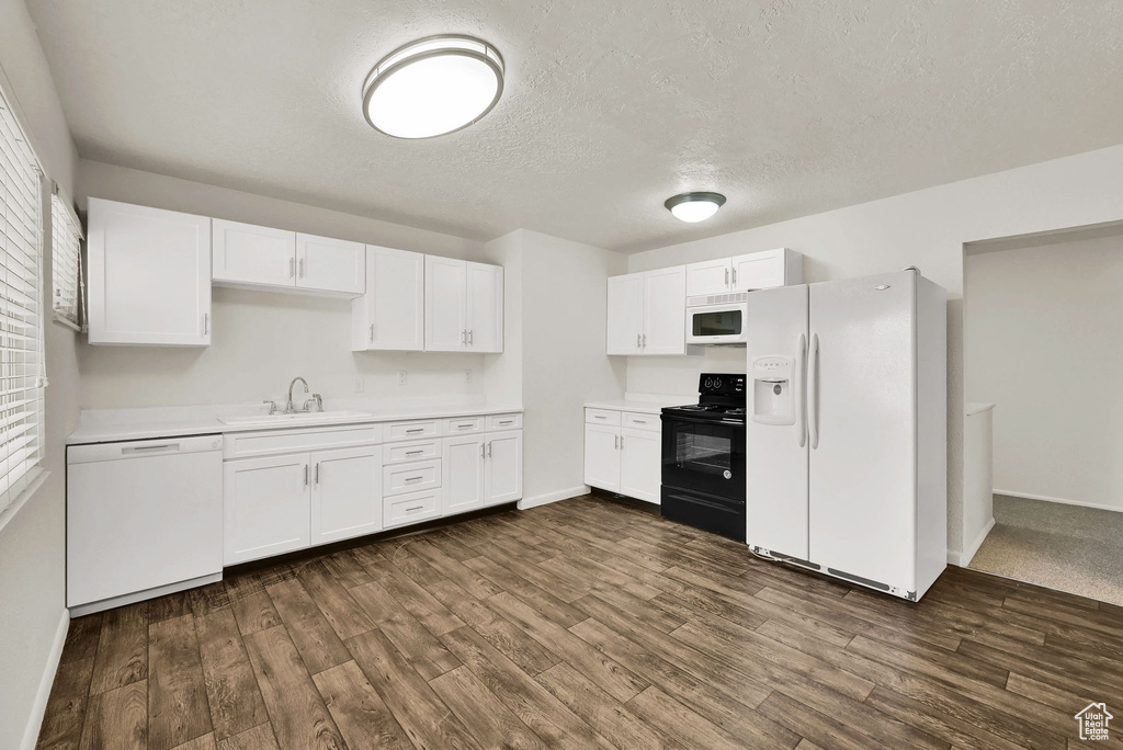 Kitchen with white appliances, light countertops, white cabinets, baseboards, and a textured ceiling